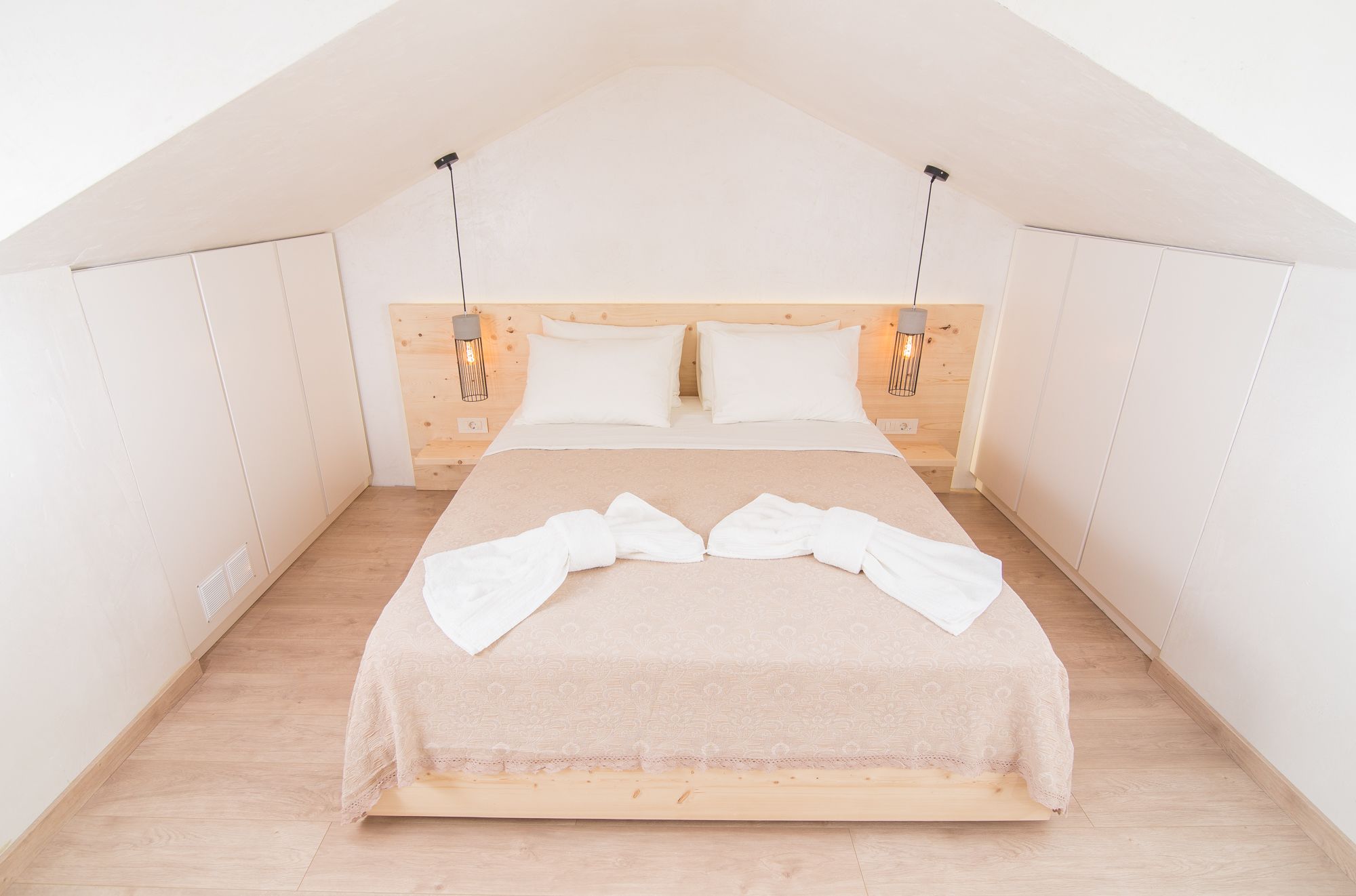 Quarto com cabeceira de madeira, duas almofadas brancas, edredom bege e um par de toalhas brancas na cama.
