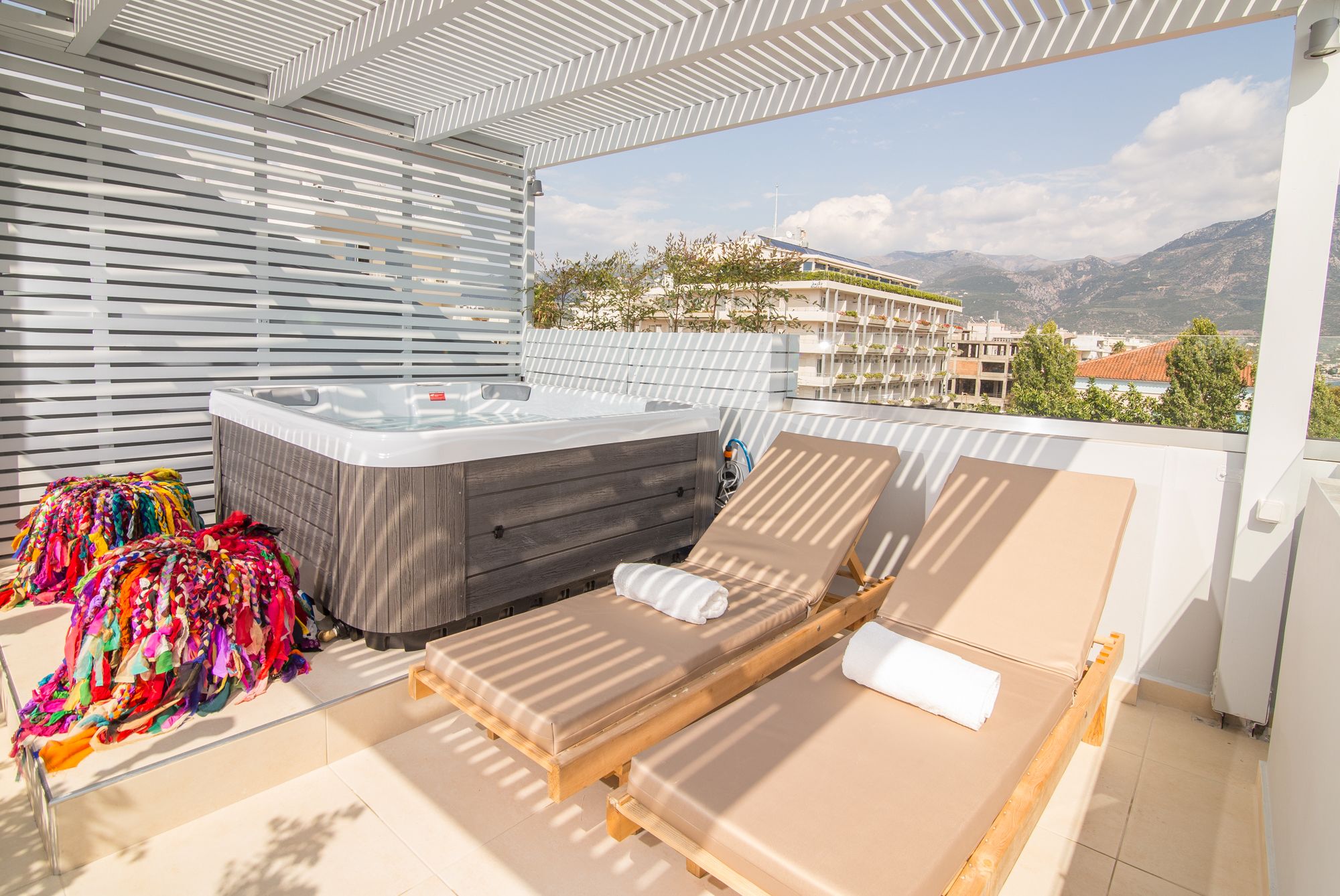 A balcony with a wooden bed, a hot tub, and colorful towels.