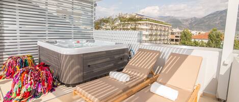 A balcony with a wooden bed, a hot tub, and colorful towels.