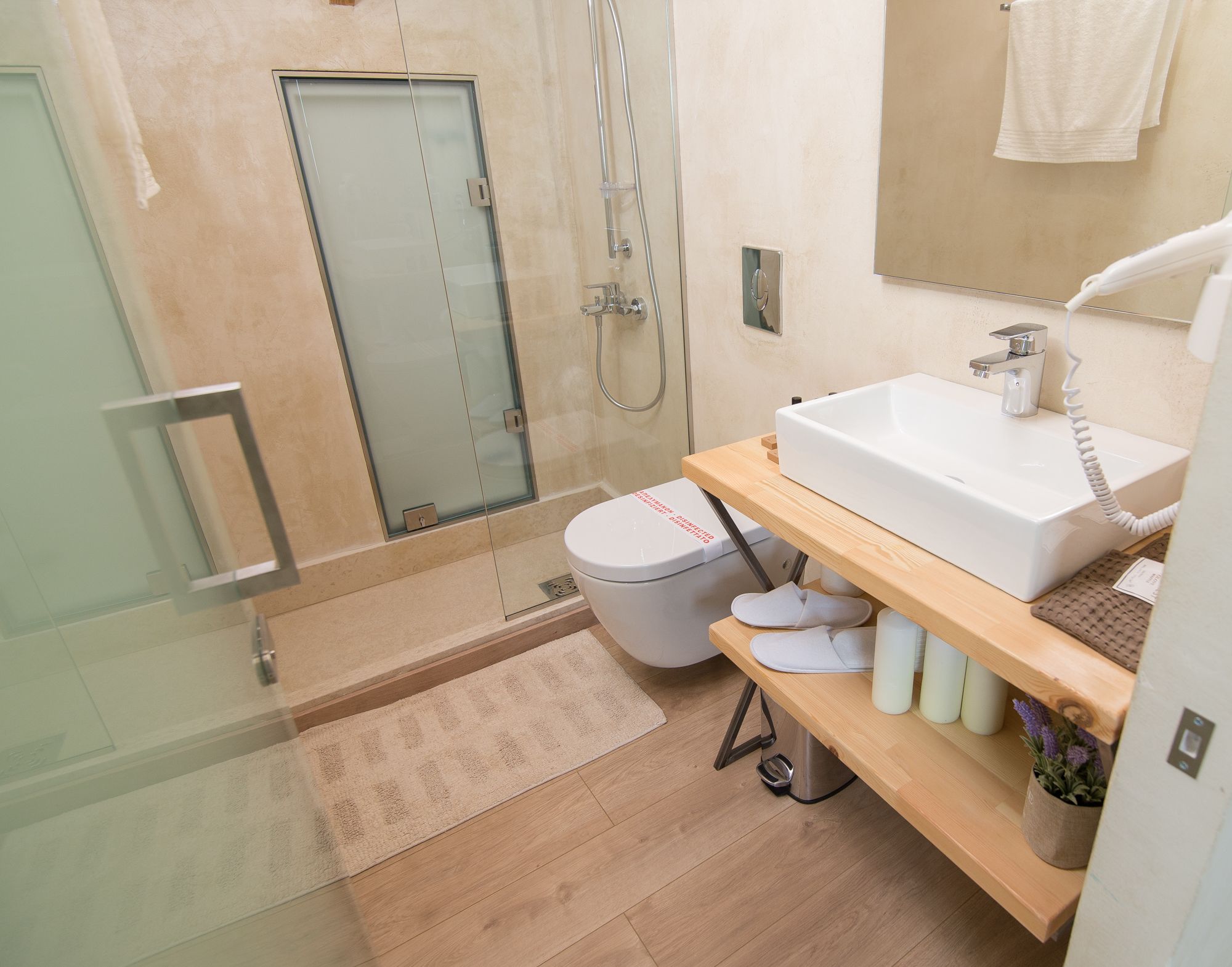 A modern bathroom with a glass shower enclosure, a white toilet, a wooden vanity with a sink, and a small potted plant.