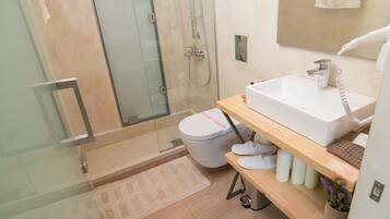 Un baño moderno con cabina de ducha de vidrio, inodoro blanco, tocador de madera con lavamanos y una pequeña planta en maceta.