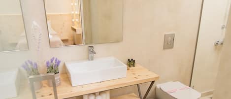 Un baño moderno con un lavabo de cristal, un espejo grande y una ducha.
