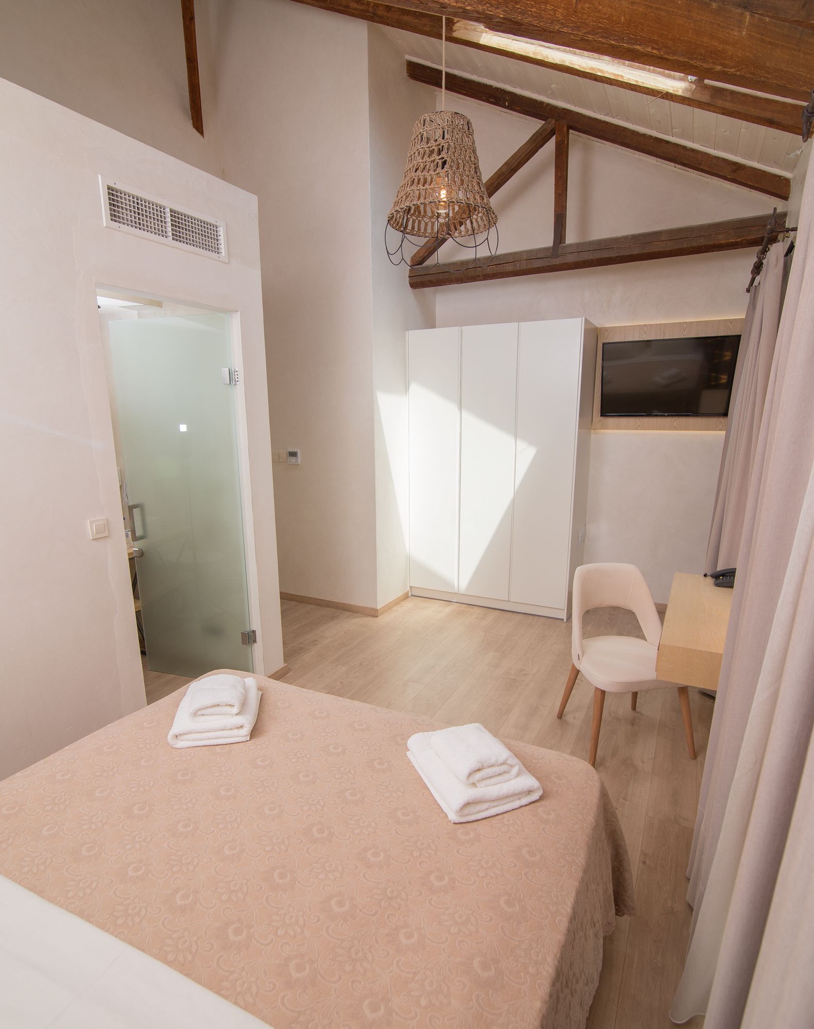 A bedroom with a bed, a chair, a desk, a TV, and a window.