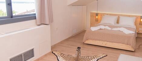A bedroom with a sloped ceiling, a large window with curtains, a bed with a headboard, and a leopard print rug.
