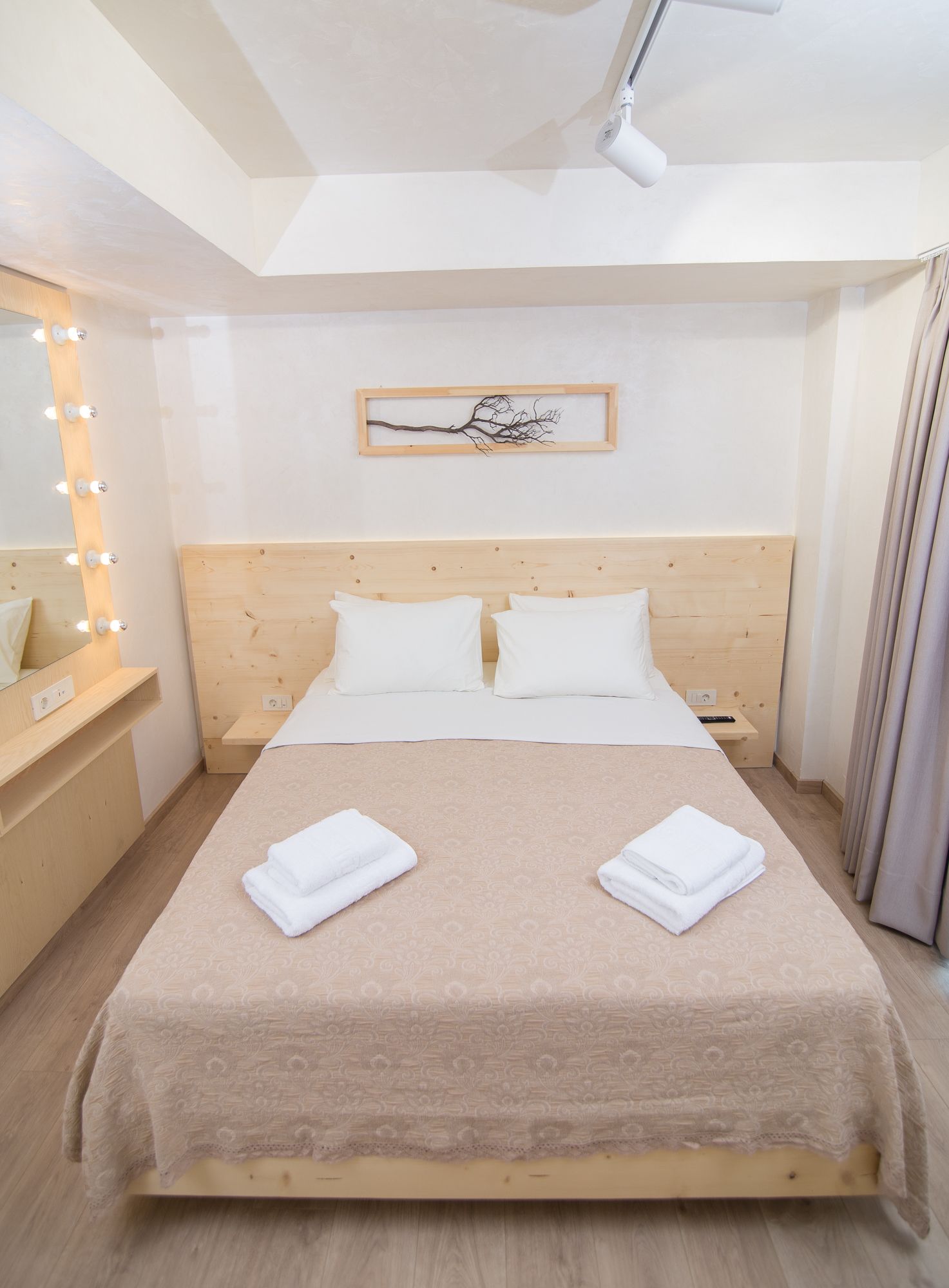 Una cama bien tendida con sábanas blancas, cabecera de madera y mesita de noche con lámpara.