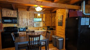 Une cuisine rustique aménagée dans une cabane en bois, avec une table à manger, des chaises, un réfrigérateur, une cuisinière, un four à micro-ondes et un évier.