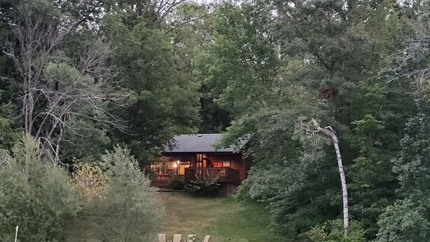 Une cabane entourée d’une forêt dense, avec une jetée qui s’avance sur un lac paisible.