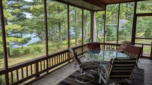 Un espace extérieur abrité, avec une table et des chaises en verre, offrant une vue sur un lac et une forêt.