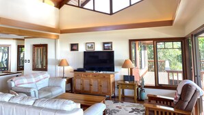 A spacious living room with a high ceiling, wooden beams, a large TV, and comfortable seating.