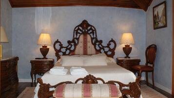 Un dormitorio tradicional con una cama grande, dos mesitas de noche, una silla de madera y un cuadro en la pared.