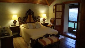 A bedroom with a wooden ceiling, a large bed with two bedside lamps, a chair, and a view through an open door. - Posada el Mirador (Soba)