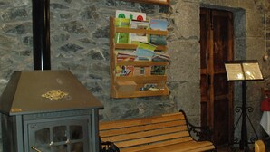 A rustic room with a stone wall, a wooden bench, a bookshelf, and a stove. - Posada el Mirador (Soba)