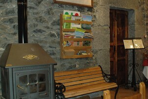 Una habitación rústica con pared de piedra, un banco de madera, una estantería y una estufa.