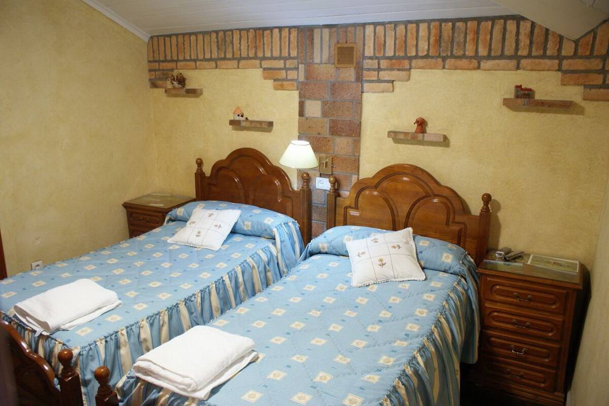 A room with two wooden beds, each with a headboard, a bedside table, and a lamp. The walls have a brick pattern design.