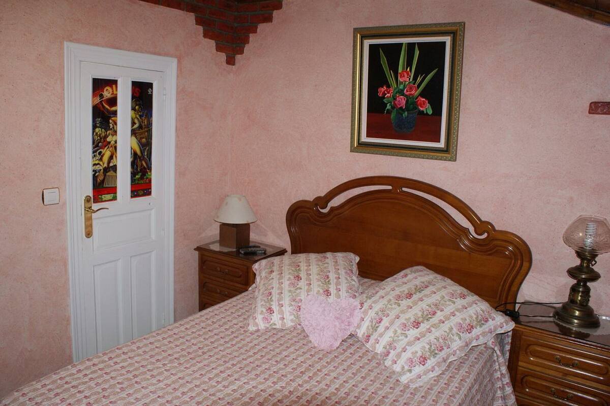 A bedroom with a wooden bed, floral bedding, a nightstand with a lamp, a framed picture on the wall, and a door with a stained glass window.
