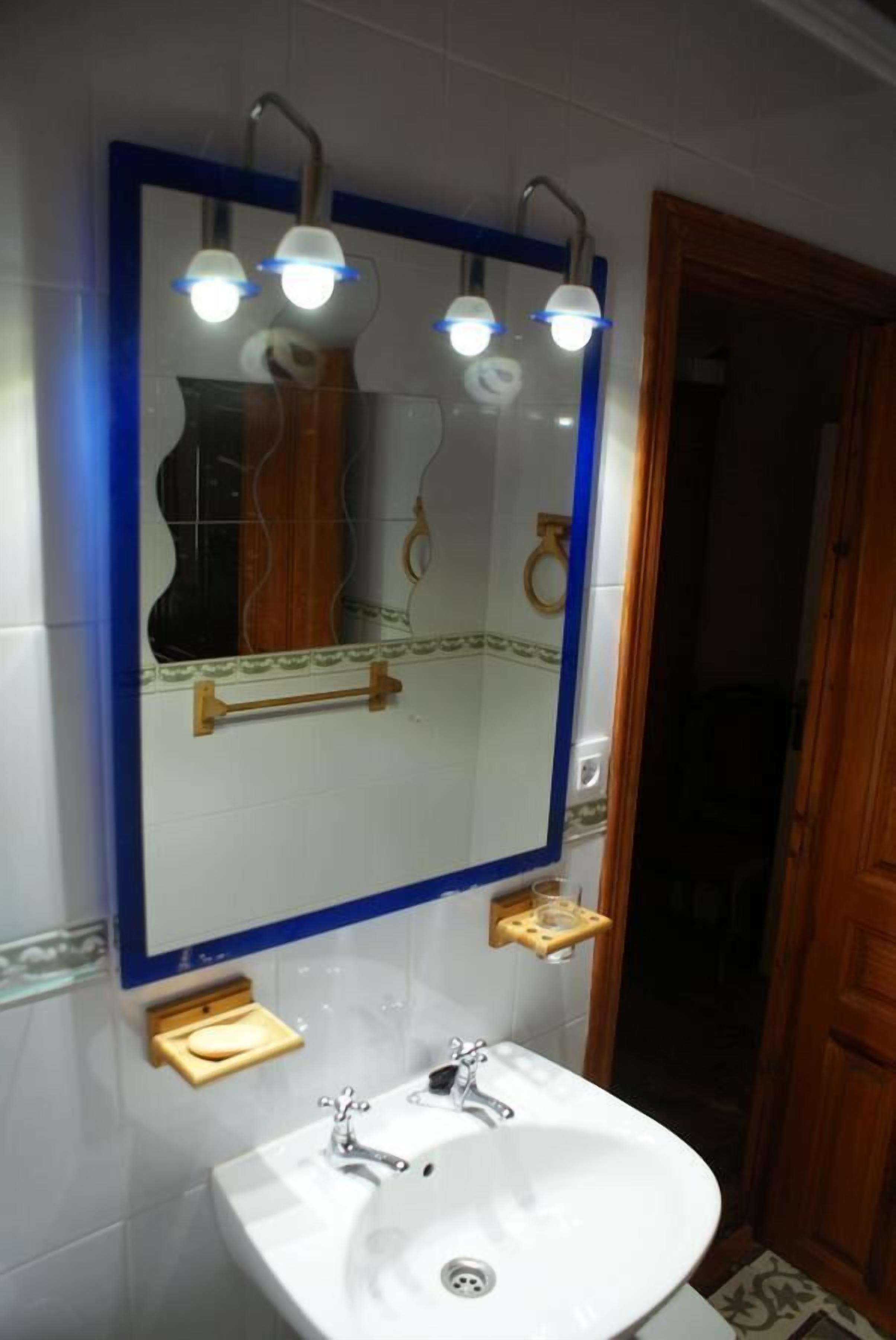 Un bagno con un lavandino bianco, uno specchio con cornice blu e tre luci sopra lo specchio.