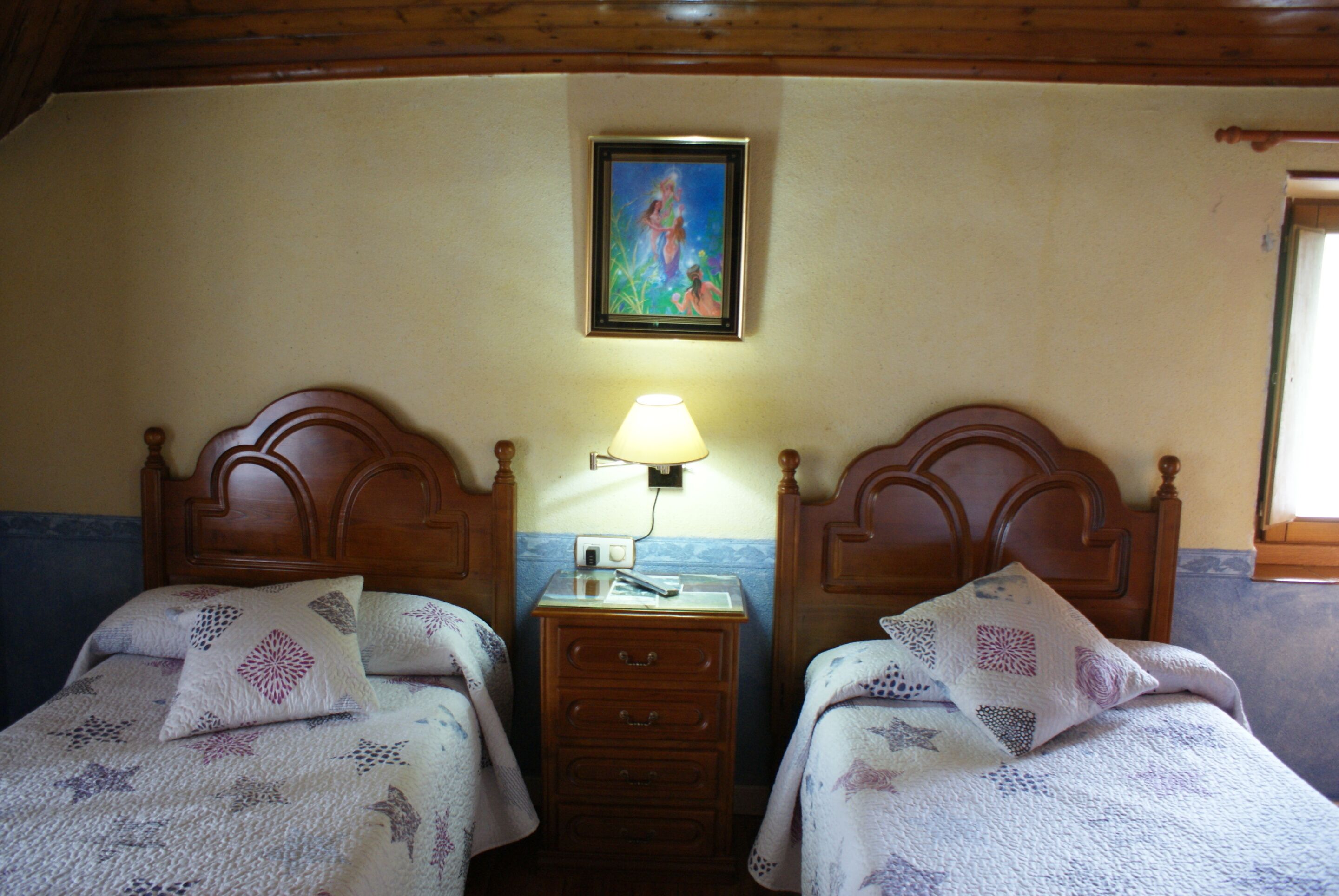 Ein Schlafzimmer mit zwei hölzernen Betten, einem Nachttisch mit Lampe und einem gerahmten Bild an der Wand.
