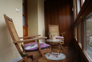 Habitación de esquina con dos sillas de madera, una con cojín, y una mesita con una planta.