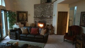 A cozy living room with a fireplace, a leather sofa, a wooden coffee table, and a large plant. - Secluded large home. Wooded setting. Easy commute to downtown.  (Portland)