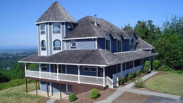 A large, two-story house with a prominent tower and a wrap-around porch. - Secluded large home. Wooded setting. Easy commute to downtown.  (Portland)