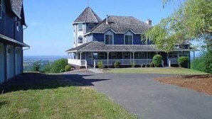 A large, two-story house with a prominent tower and a wrap-around porch. - Secluded large home. Wooded setting. Easy commute to downtown.  (Portland)
