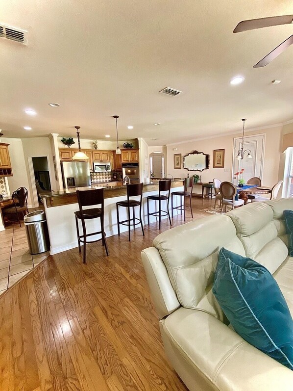 A spacious living area with a leather sofa, wooden flooring, and a kitchen area with wooden cabinets and modern appliances.