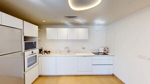 Une cuisine moderne avec des meubles blancs, un four encastré, un micro-ondes, un évier et un plan de travail sur lequel se trouvent une bouilloire et un livre de recettes.