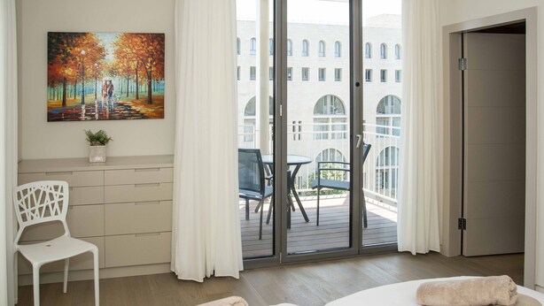 Une chambre d’hôtel avec deux lits, un tableau, une chaise et un balcon donnant sur des immeubles.
