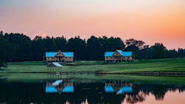 Two wooden cabins with blue roofs, a dock, and a calm lake reflecting the structures. - Rural Respite & Retreat Area (Fitzpatrick)
