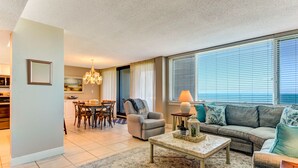 A spacious living room with a sofa, armchair, and coffee table, a dining area with chairs and a table, and a kitchen in the background. - Beautiful Oceanfront, 3br/2ba Beachwalker (Amelia Island)