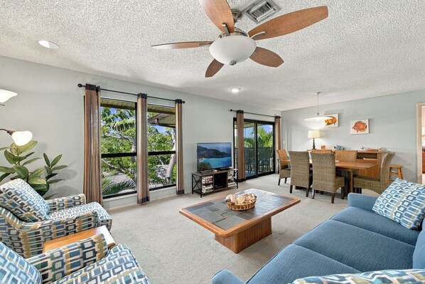 A spacious living area with a ceiling fan, a television, and a dining area with wicker furniture.