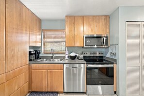 A compact kitchen with wooden cabinets, a stainless steel dishwasher, a microwave, a stove, and a sink.