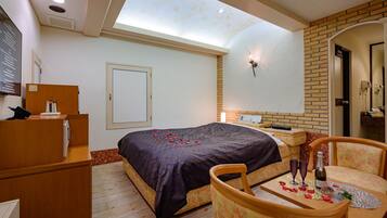 Un dormitorio con cama, escritorio, silla, mesita de noche, espejo, puerta y tragaluz.