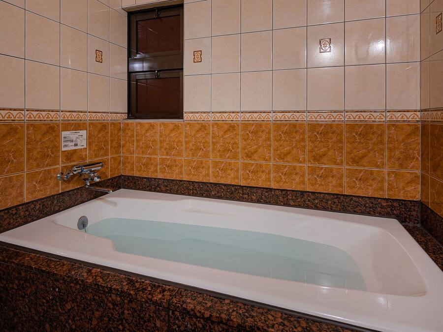 A bathroom with a bathtub, marble tiles, and a shower area.