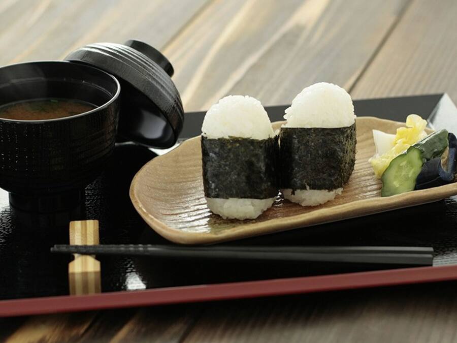 Uma refeição tradicional japonesa com dois pedaços de sushi, uma tigela de sopa e um prato pequeno com legumes.