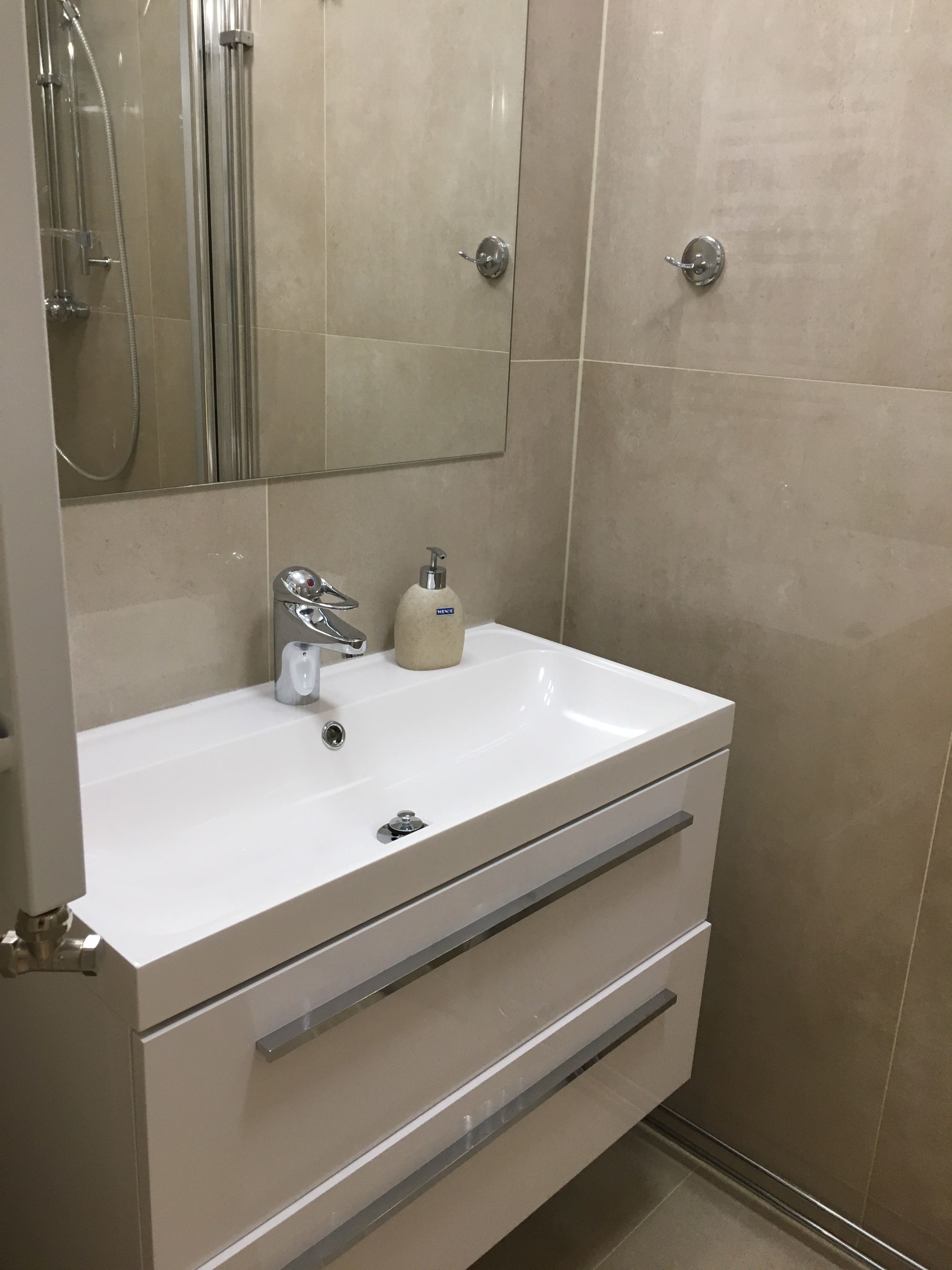 Un baño con un lavamanos blanco, un espejo y una cabina de ducha.