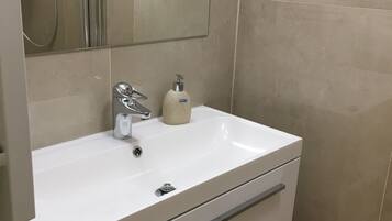 Un baño con un lavamanos blanco, un espejo y una cabina de ducha.