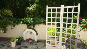A stone-paved patio with a white trellis, potted plants, and a metal chair.