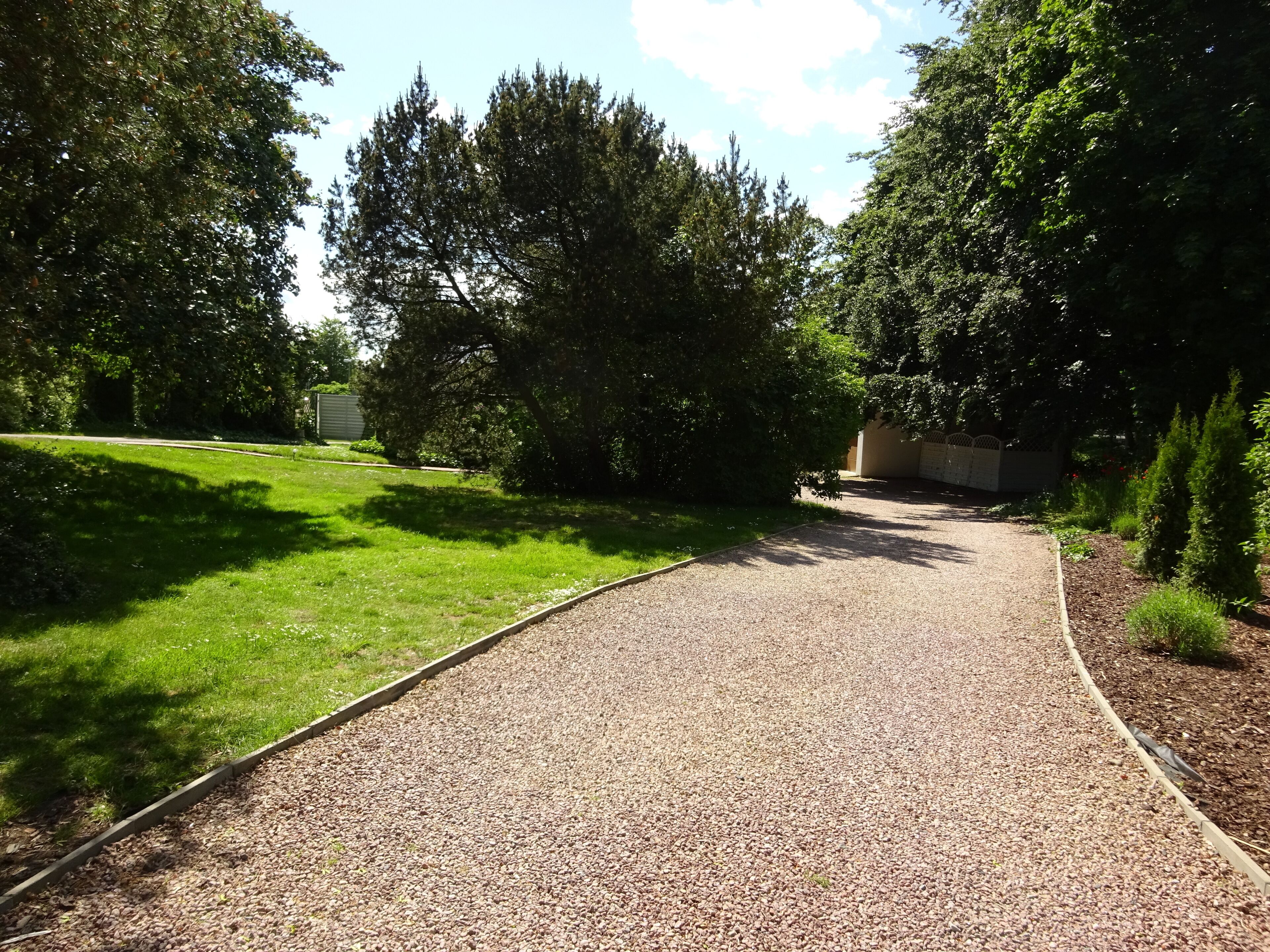 A gravel pathway in a park with green grass and trees.