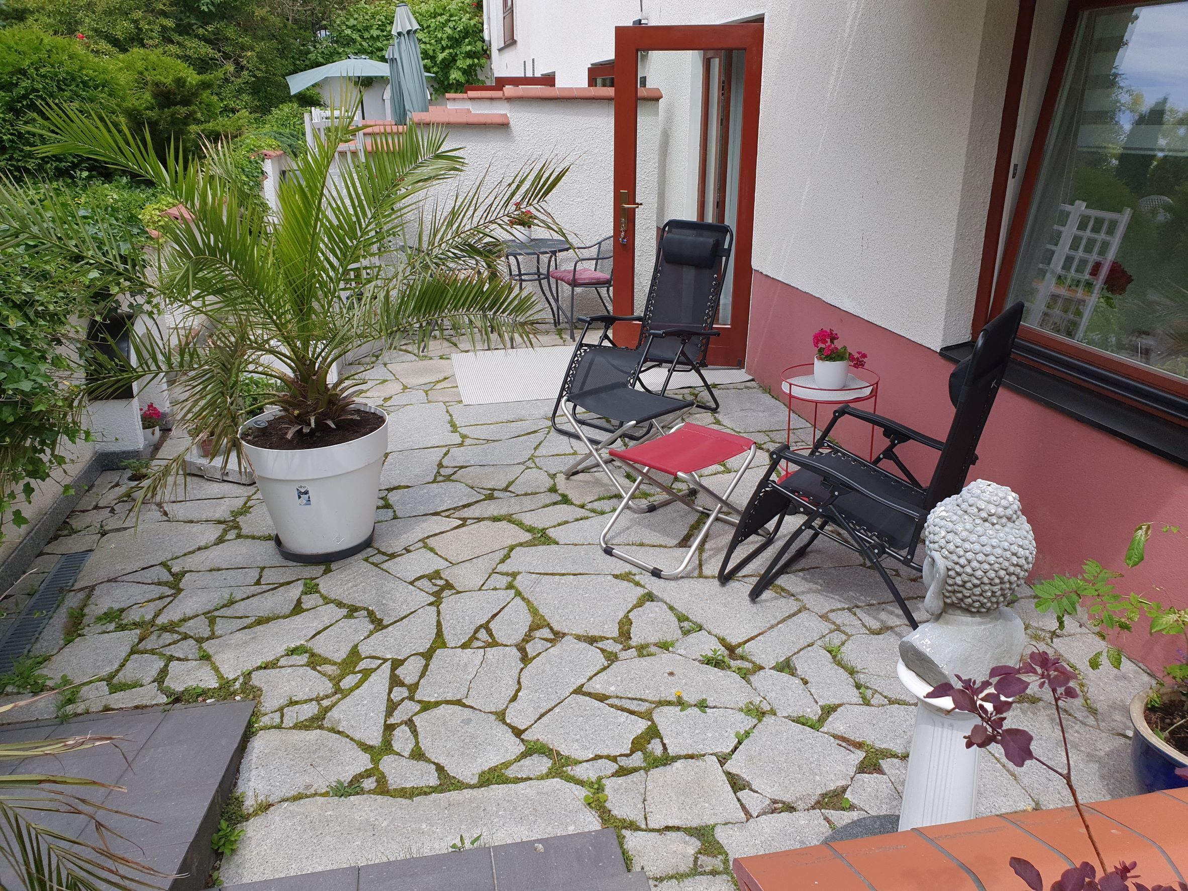 Un patio con suelo de piedra, mobiliario exterior y plantas en macetas.