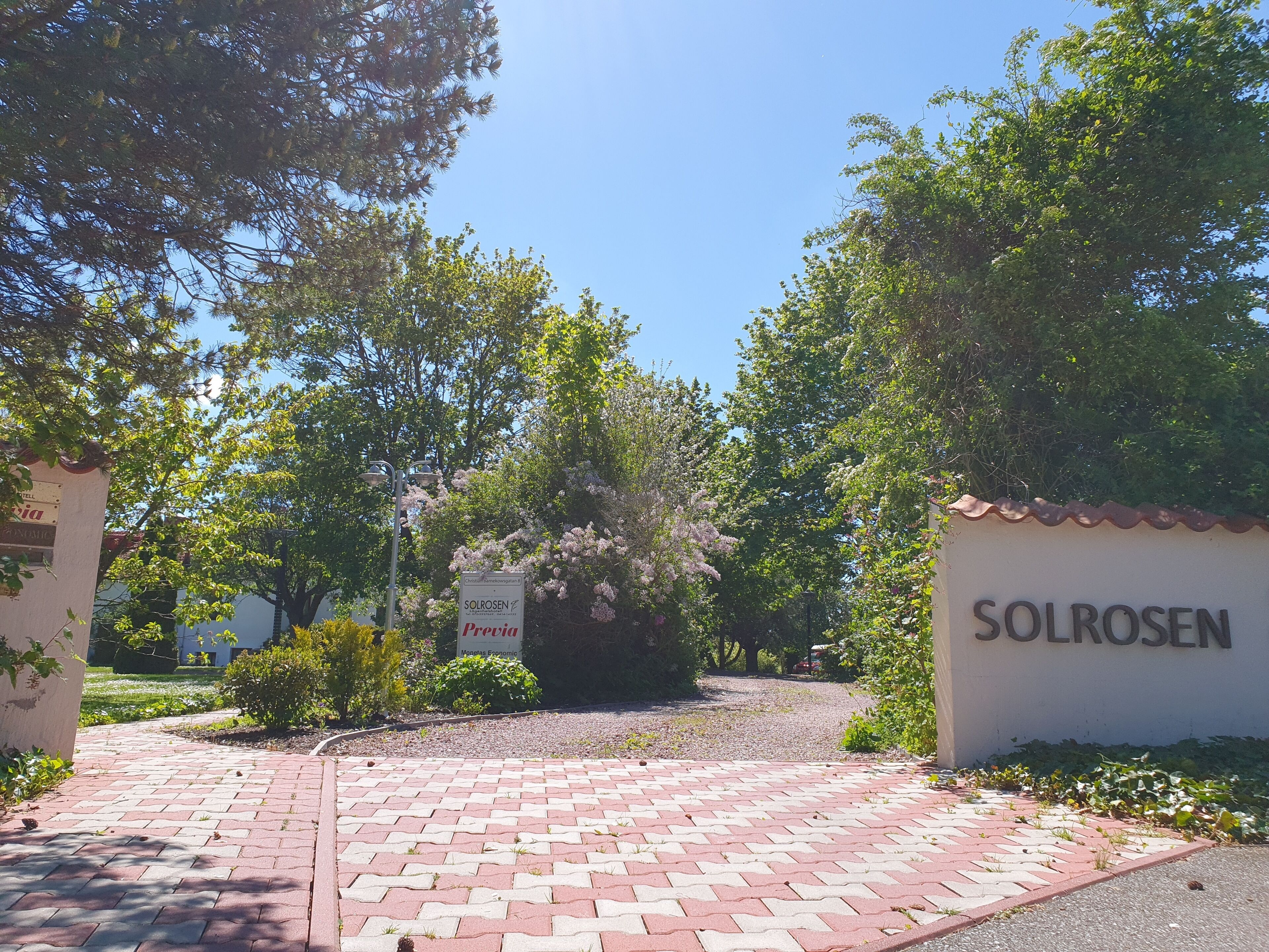 Una entrada pavimentada con un cartel que dice "Solrosen" y un anuncio para "Monedas, Economic".