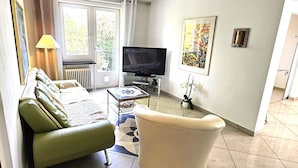 A living room with a sofa, armchair, TV, and artwork on the wall.