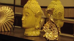 A collection of decorative items on a shelf, including a Buddha head sculpture and a golden ornamental piece. - Eddison Hotel (Gurugram)