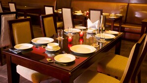 A restaurant dining area with tables set for four, each with plates, cutlery, and candles. - Eddison Hotel (Gurugram)