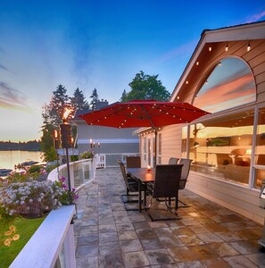 A patio with stone flooring, a table with chairs, a red umbrella, and a view of the water and trees. - Lakefront Home-4 Bedrooms, 3 Full Bathrooms-Sleeps 10+ Hot Tub and Kayaks  (Bremerton)