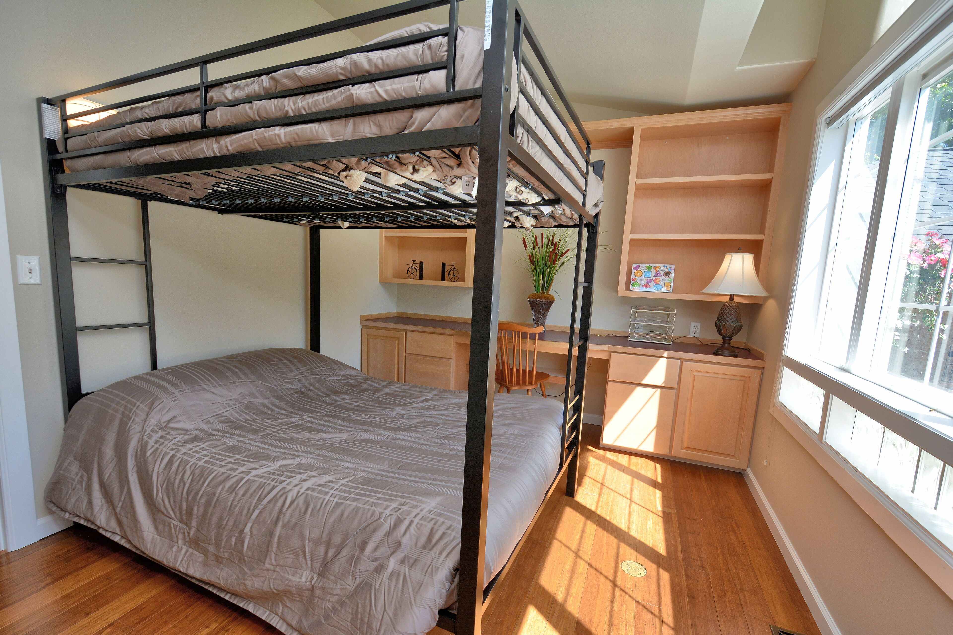 A bunk bed with a desk and shelves, a window with a view, and a plant on the desk.
