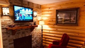 A cozy log cabin interior with a stone fireplace, a mounted television, and a red armchair. - Downtown, nice furnishings, clean and cozy w/ fireplace, indoor & outdoor pools. (Gatlinburg)