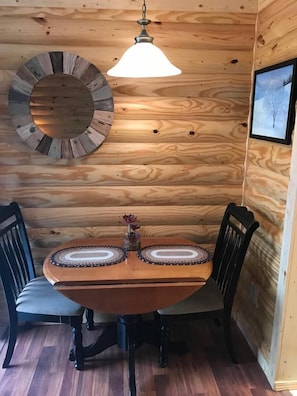 A dining area with a round table for two, two chairs, and a pendant light.