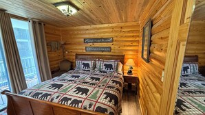 A wooden cabin bedroom with a bed, two nightstands, a bench, and a window with curtains. - Downtown, nice furnishings, clean and cozy w/ fireplace, indoor & outdoor pools. (Gatlinburg)