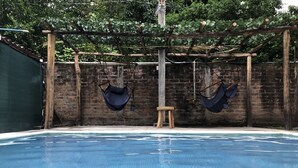 Une piscine avec deux hamacs suspendus et un tabouret en bois.